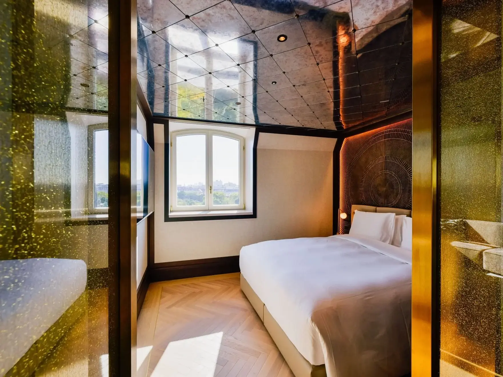 Experience the Almanac Park Suite: a modern hotel room with a large bed, decorative wall, mirrored ceiling, wooden floors, and a window offering stunning city views.