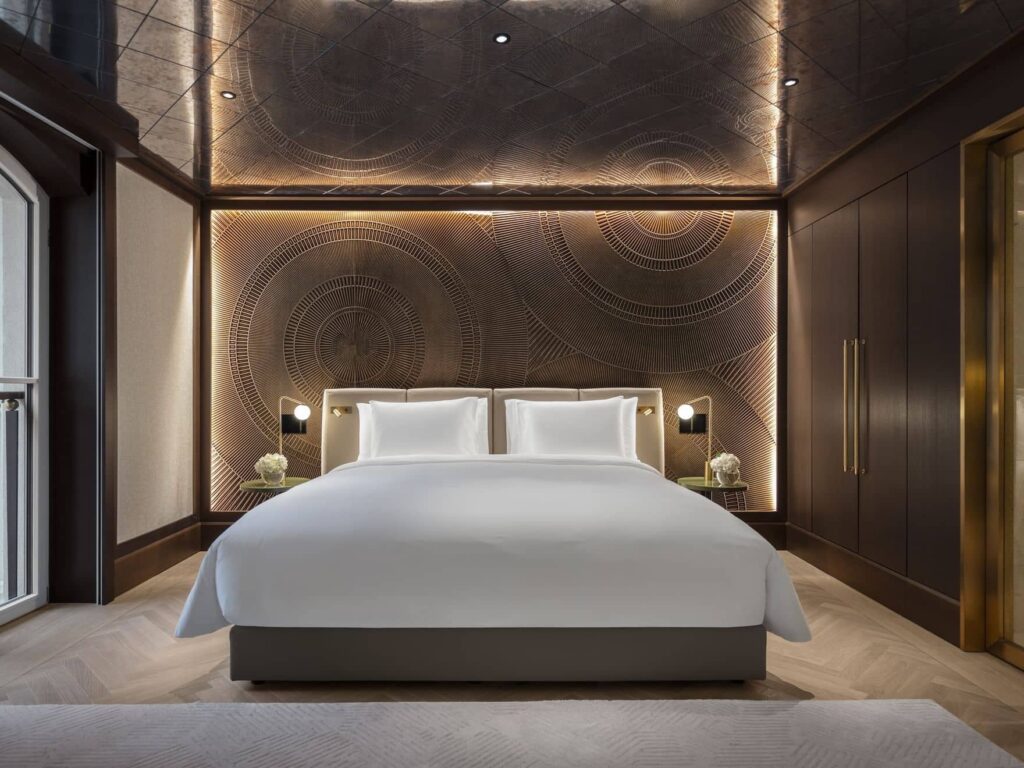 Modernes Palais Etage-Hotelzimmer mit einem sauber gemachten Doppelbett, weißer Bettwäsche, dekorativen Wandpaneelen, eingebauter Beleuchtung und dunklen Holzakzenten.