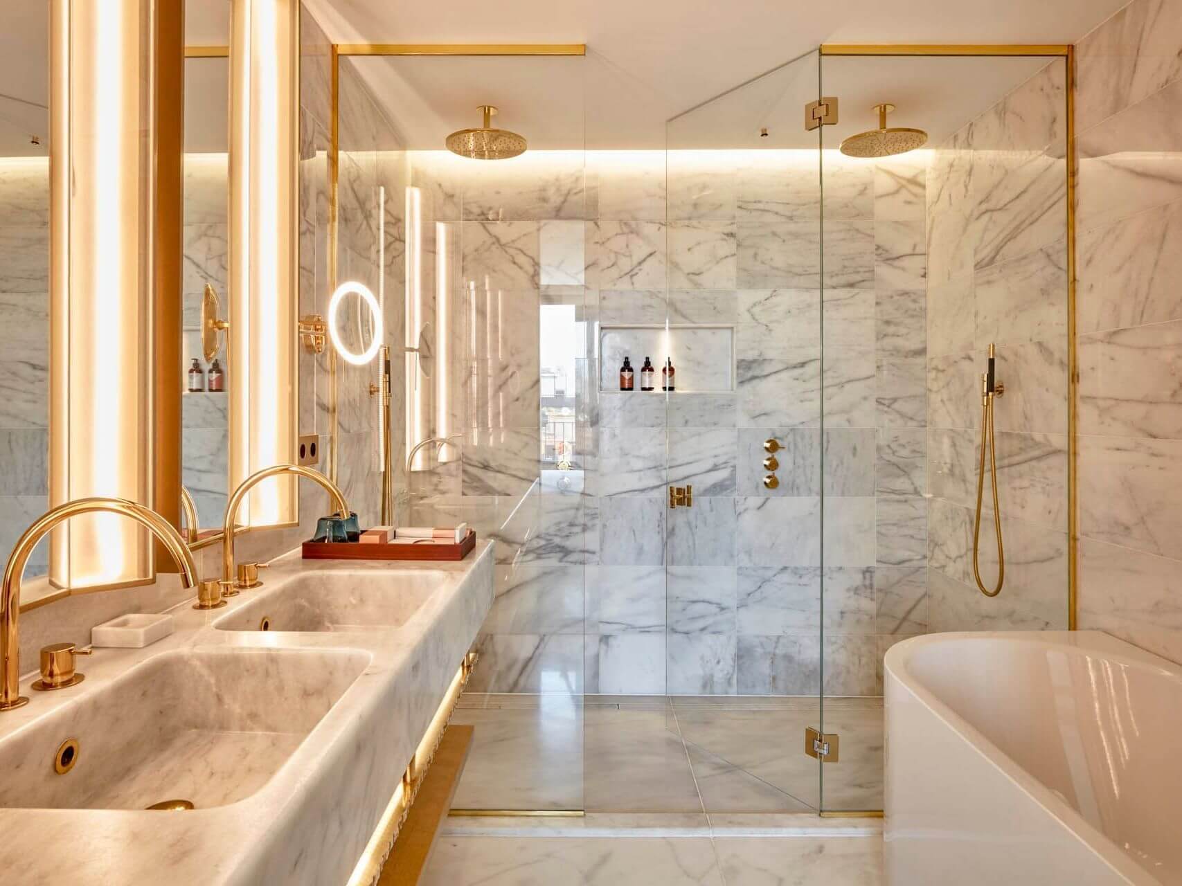Bany suite a l'àtic amb parets i terres de marbre, lavabo doble amb accessoris daurats, mampara de dutxa de vidre i banyera independent: un luxe perfecte per a dues habitacions.