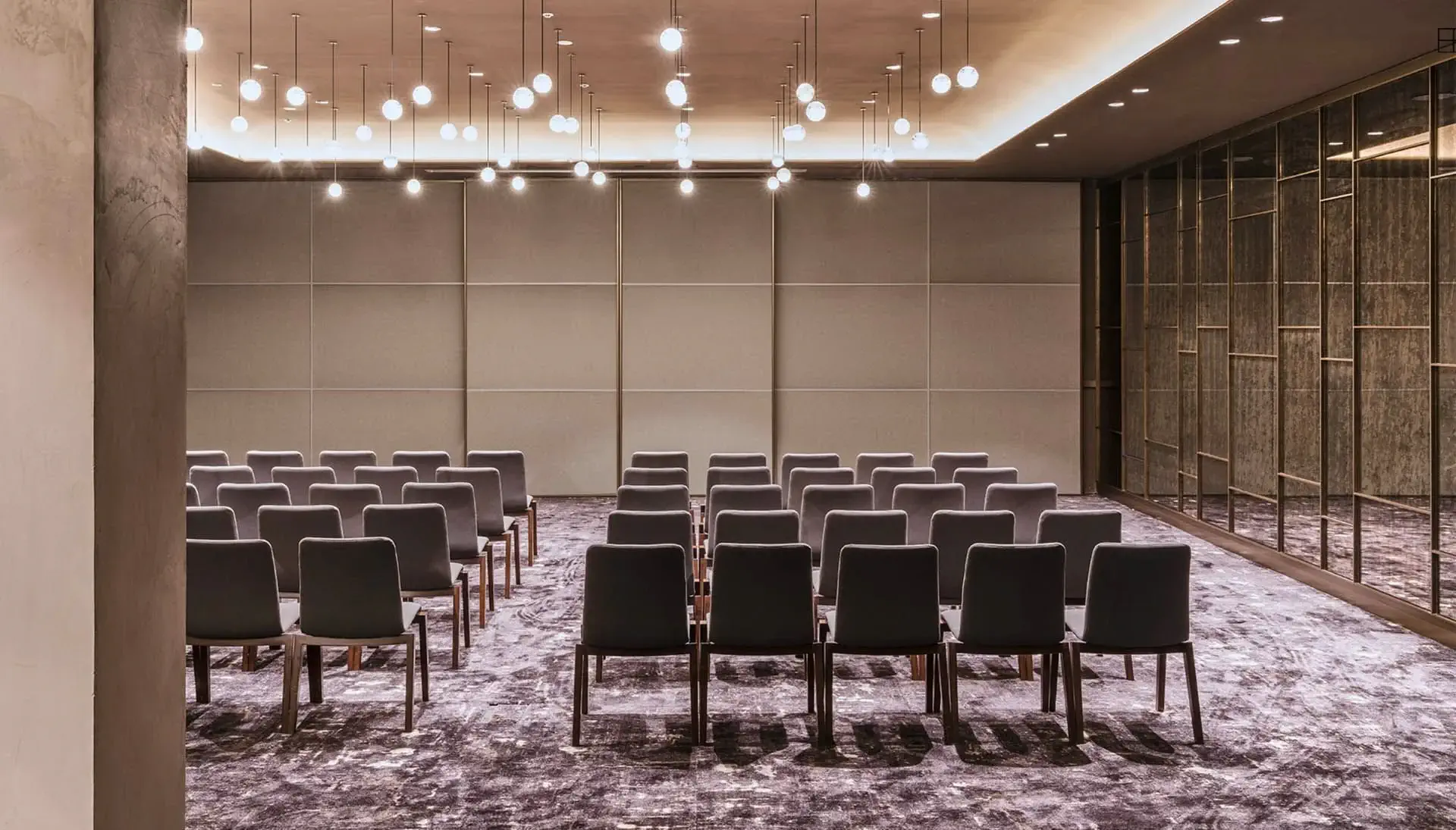 A modern conference room with rows of empty chairs facing a blank wall, illuminated by ceiling lights—perfect for group meetings or social events.
