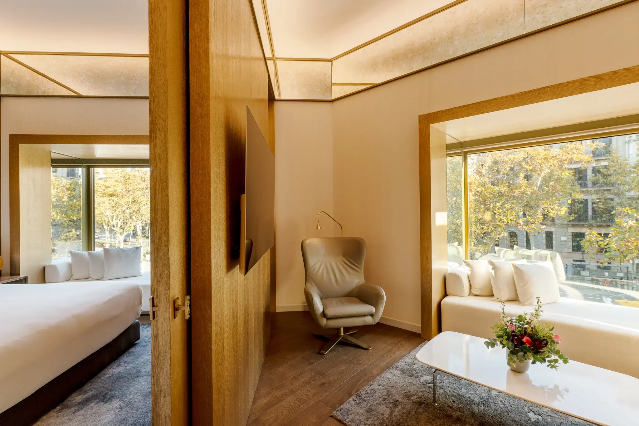 Moderne Almanac Suite mit Bett, Sessel, weißem Sofa, Couchtisch mit Blumen, großen Fenstern und neutralem Dekor - ideal für Gäste, die luxuriösen Komfort in zwei Schlafzimmern suchen.