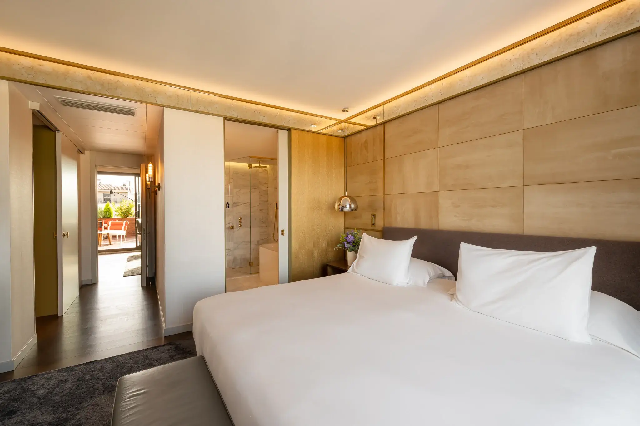 Modern Grand Penthouse Suite featuring a large bed, wall-mounted reading lamps, marble-accented open bathroom, and a terrace visible through the hallway.