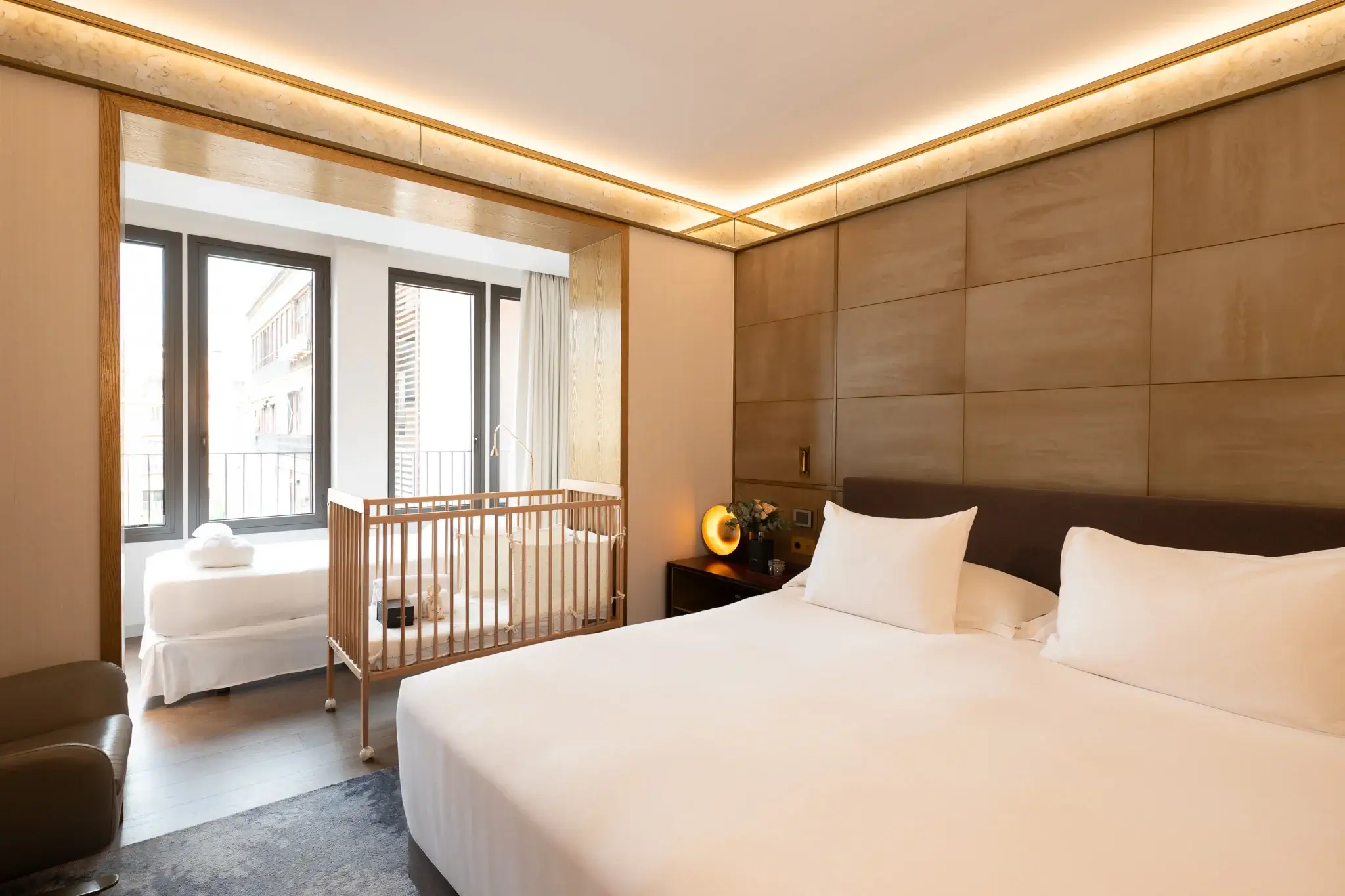 Moderna habitación de hotel con una gran cama doble, una cuna, una cama individual cerca de la ventana y una cálida iluminación ambiental.