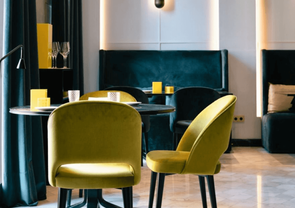 Un interior modern del restaurant Virens amb cadires de vellut verd, una taula rodona, seients foscos en forma de reserva, detalls de decoració grocs i il·luminació suau.