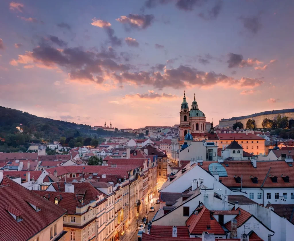 Stadtbild bei Sonnenuntergang mit roten Ziegeldächern, historischen Gebäuden und einer großen Kirche mit Zwillingstürmen unter einem bunten Himmel - eine inspirierende Raumgestaltung für Liebhaber historischer Architektur.
