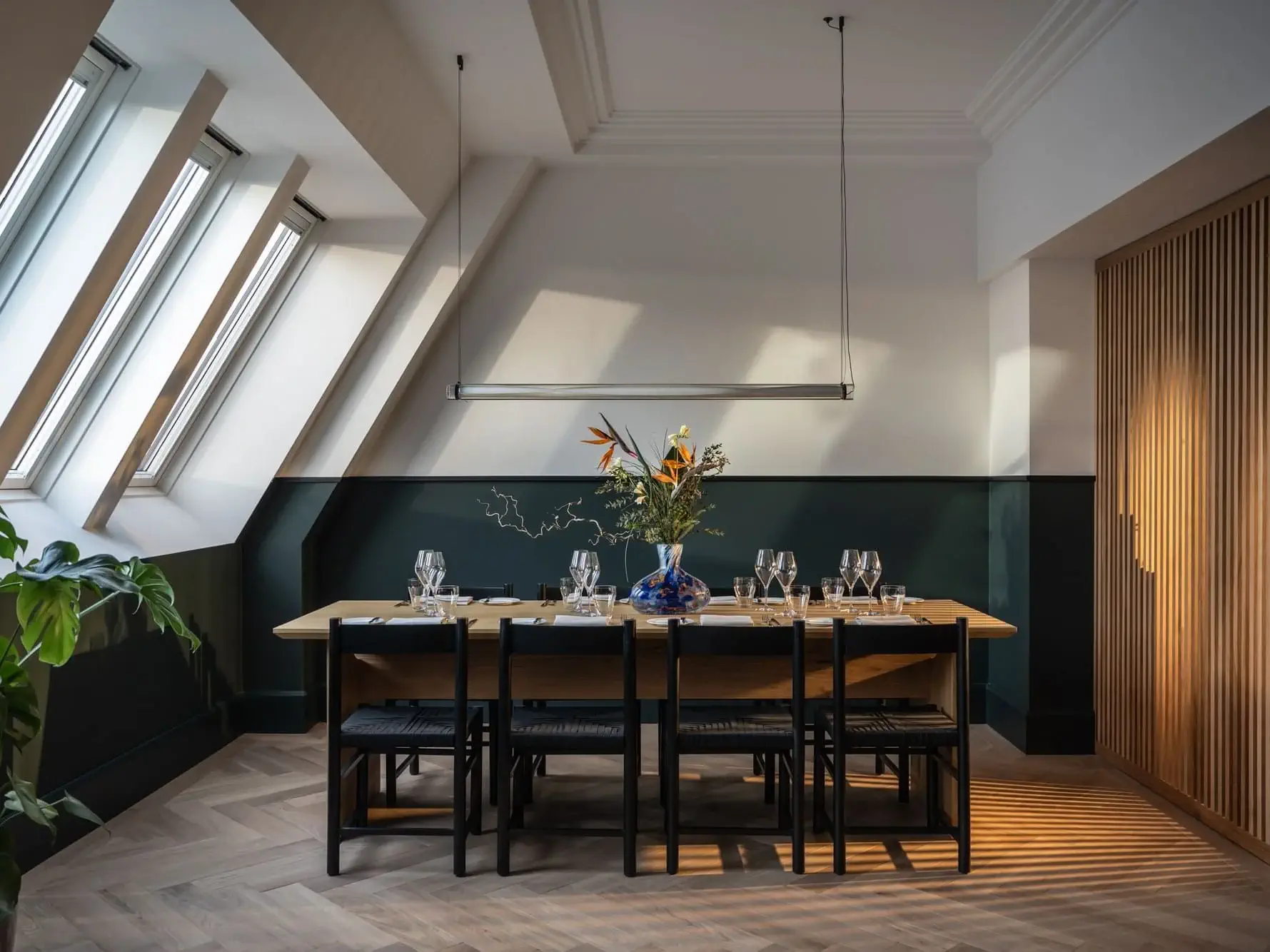 Ein modernes Esszimmer im Stil der Präsidentensuite verfügt über einen Holztisch für sechs Personen, schwarze Stühle, einen Blumenschmuck in der Mitte, schräge Oberlichter und ein minimalistisches Dekor.