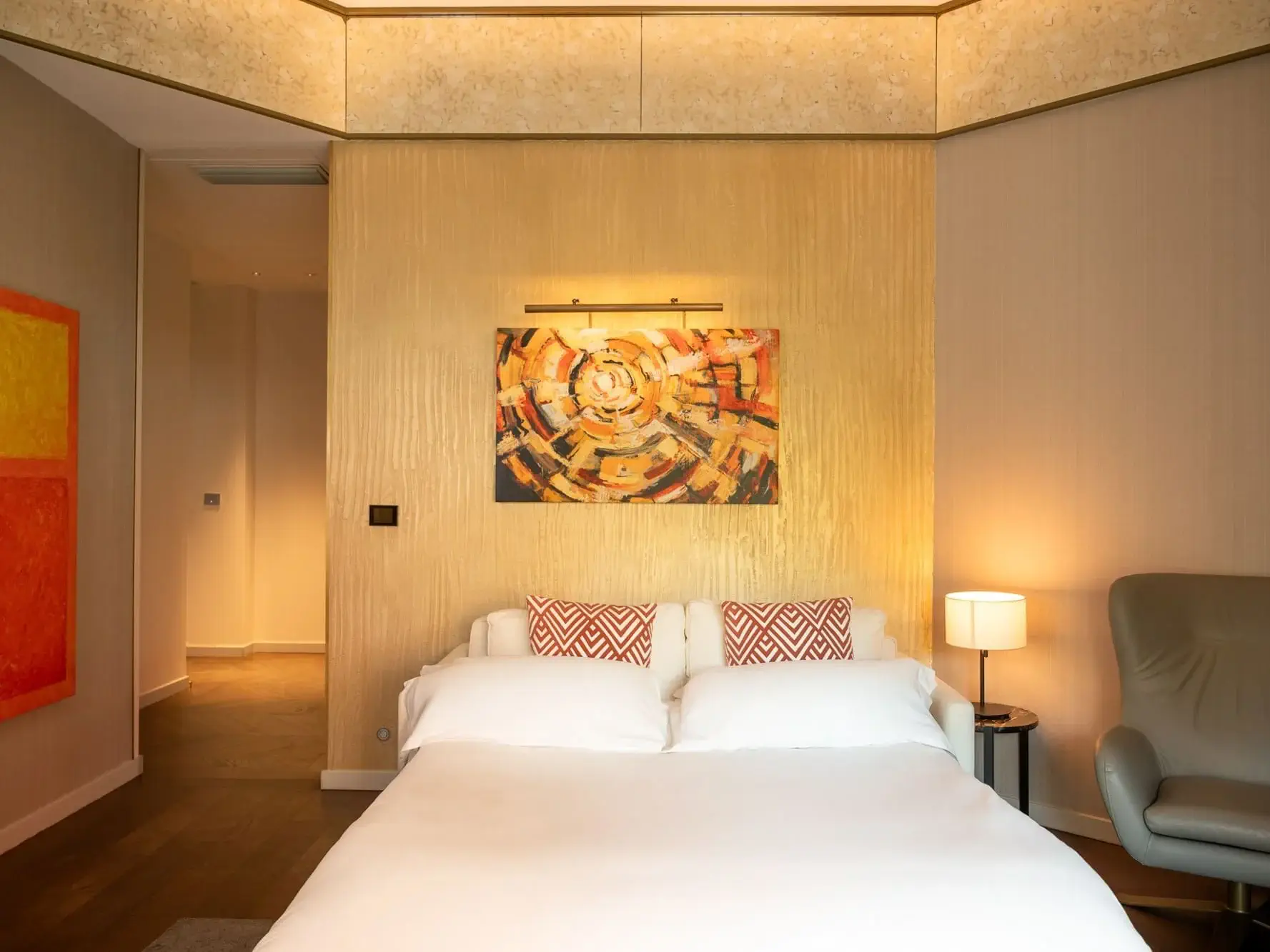 Modernes Schlafzimmer in der Almanac Family Suite mit einem Doppelbett, gemusterten Kissen, einem abstrakten Kunstwerk über dem Kopfteil, einer Nachttischlampe und einem Sessel in einem warm beleuchteten Raum.