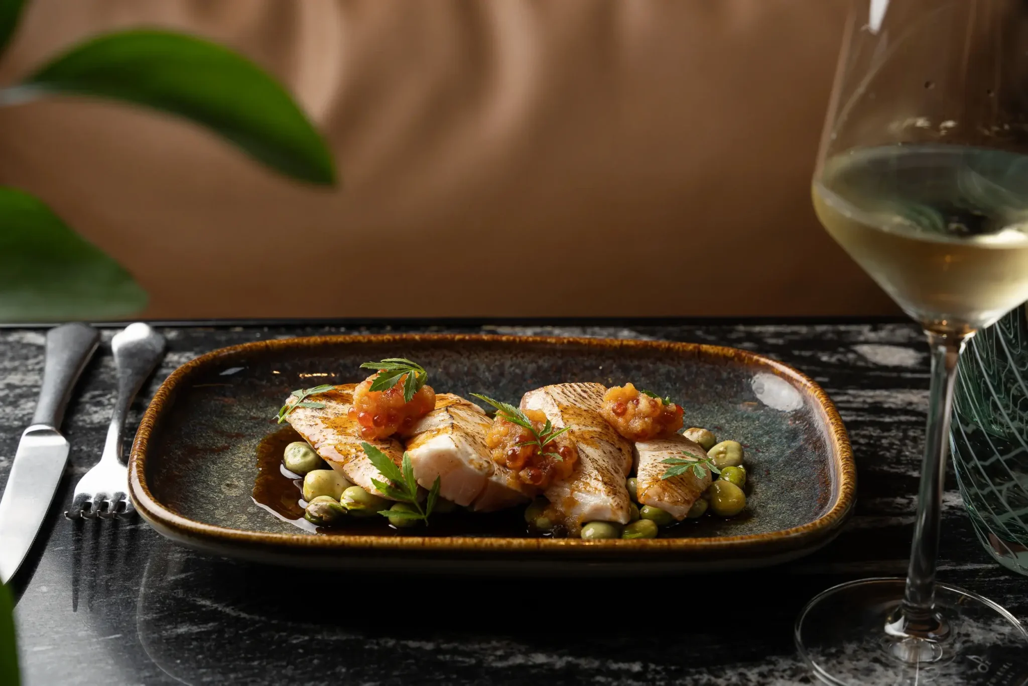 Filets de peix a la planxa amb una salsa de tomàquet, servits sobre un llit de mongetes verdes, al costat d'una copa de vi blanc sobre una taula de marbre al nostre elegant restaurant.