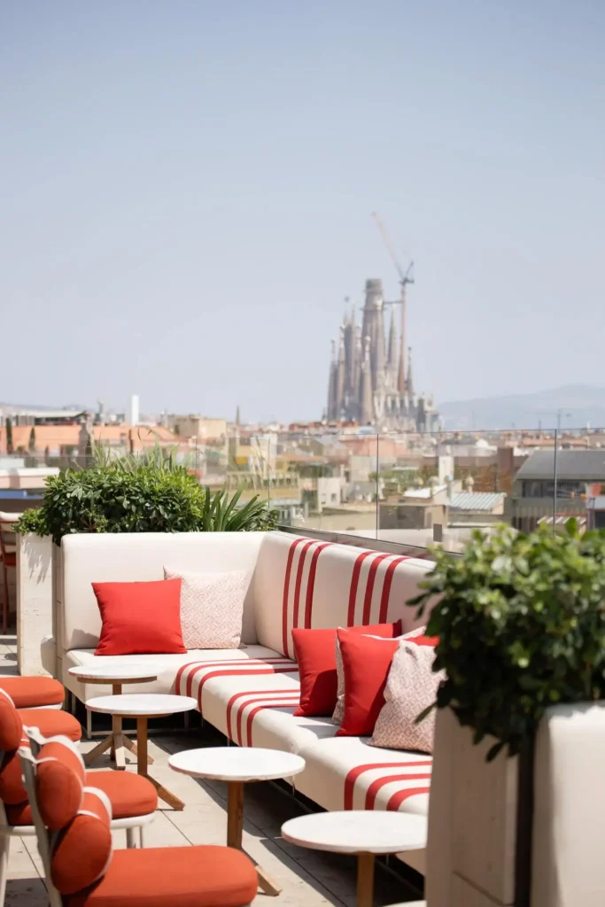 Una terrassa a la teulada de Terrassa amb seients a ratlles vermelles i blanques domina el paisatge urbà, oferint una impressionant vista azimutal d'una gran catedral i una grua de construcció distant.
