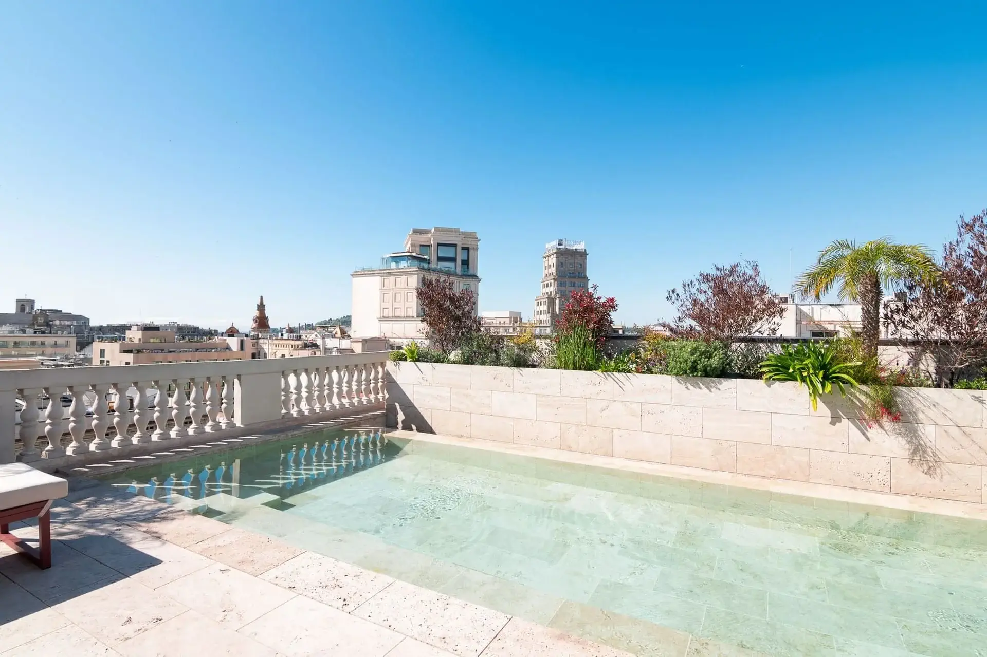 Terrassa d'estil terrassenc amb una petita piscina rectangular, rajoles de pedra, plantes exuberants i edificis de la ciutat en azimut sota un cel blau clar.