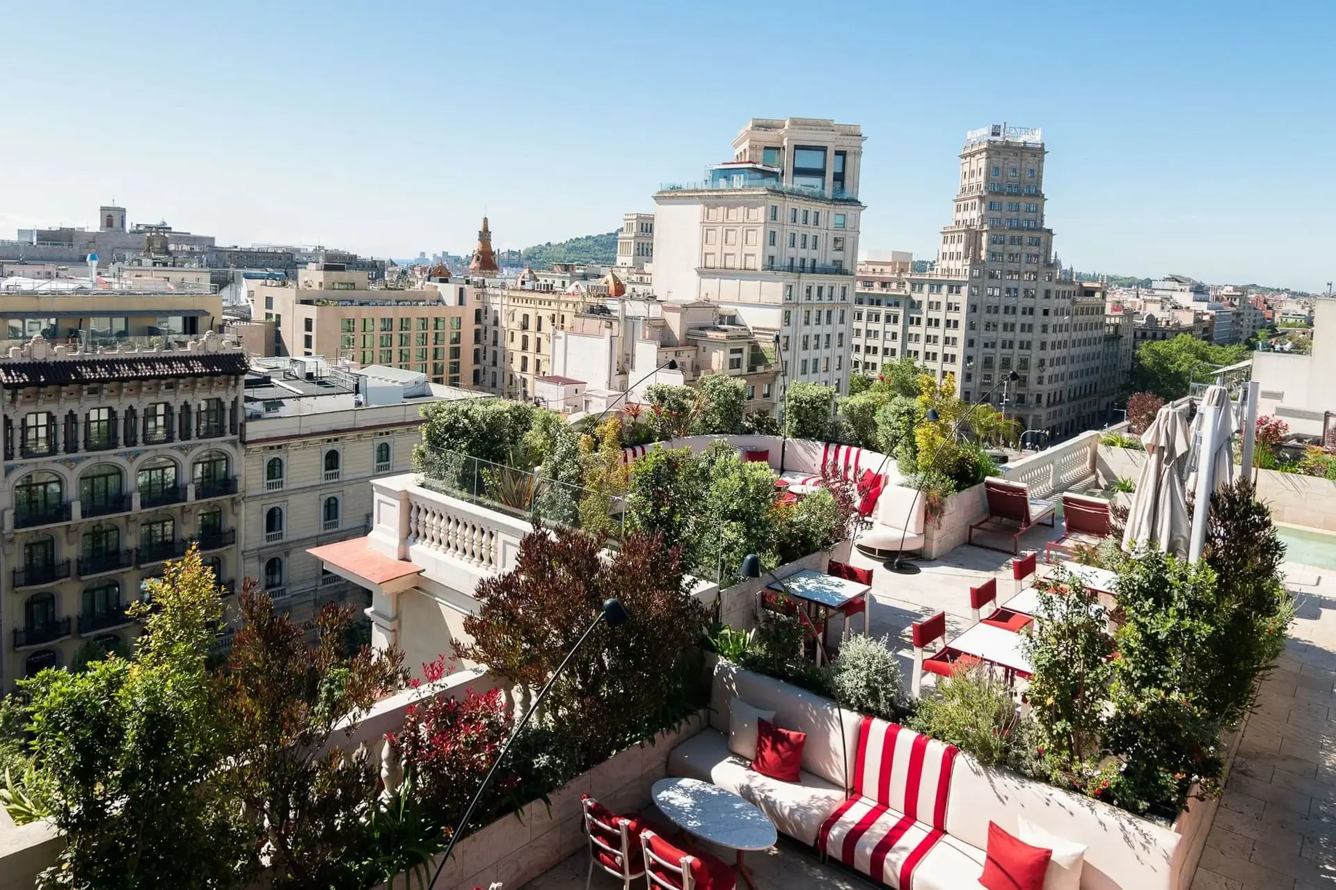 La terrassa del terrat de Terrassa, amb seients vermells i blancs, plantes en test i edificis de la ciutat al fons sota un cel blau clar, ofereix unes vistes azimutals impressionants.