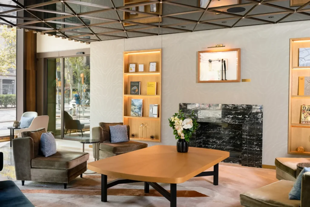 Sala d'estar moderna amb cadires de vellut marró, una taula de centre de fusta, una llar de foc de marbre negre, prestatges integrats i grans finestrals que deixen entrar llum natural, perfecta per a aquells que busquen espais inspiradors.