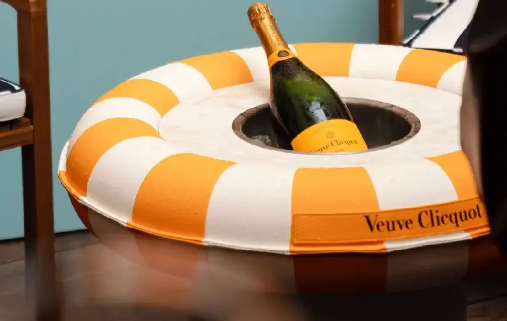 A bottle of Veuve Clicquot champagne is placed in the center of an orange and white striped lifebuoy on a table at the vibrant SUN CLUB TERRACE.