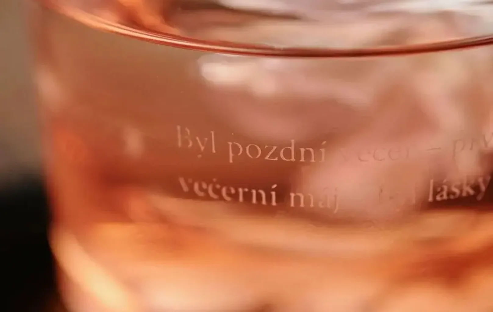 Detail sklenice s růžovou tekutinou a ledem uvnitř, s vyleptaným českým textem na povrchu - ideální pro vychutnání osvěžujícího nápoje SAKURA KOKTEJL nebo oblíbeného nápoje LINDY PRO.