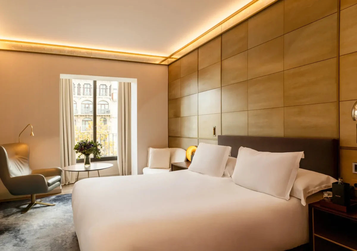Modern hotel room with a large bed, two white chairs by a window, a small round table with flowers, warm lighting, and the option for Family Connecting Rooms for added comfort and convenience.