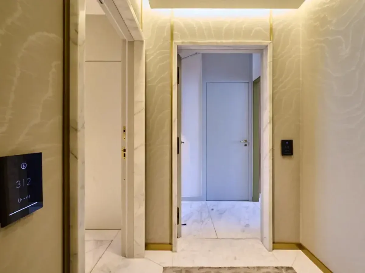 Moderno vestíbulo con suelos de mármol, paredes de color beige claro, dos puertas abiertas que dan a una sala de conexión familiar y un panel digital en la pared que muestra el número 312.