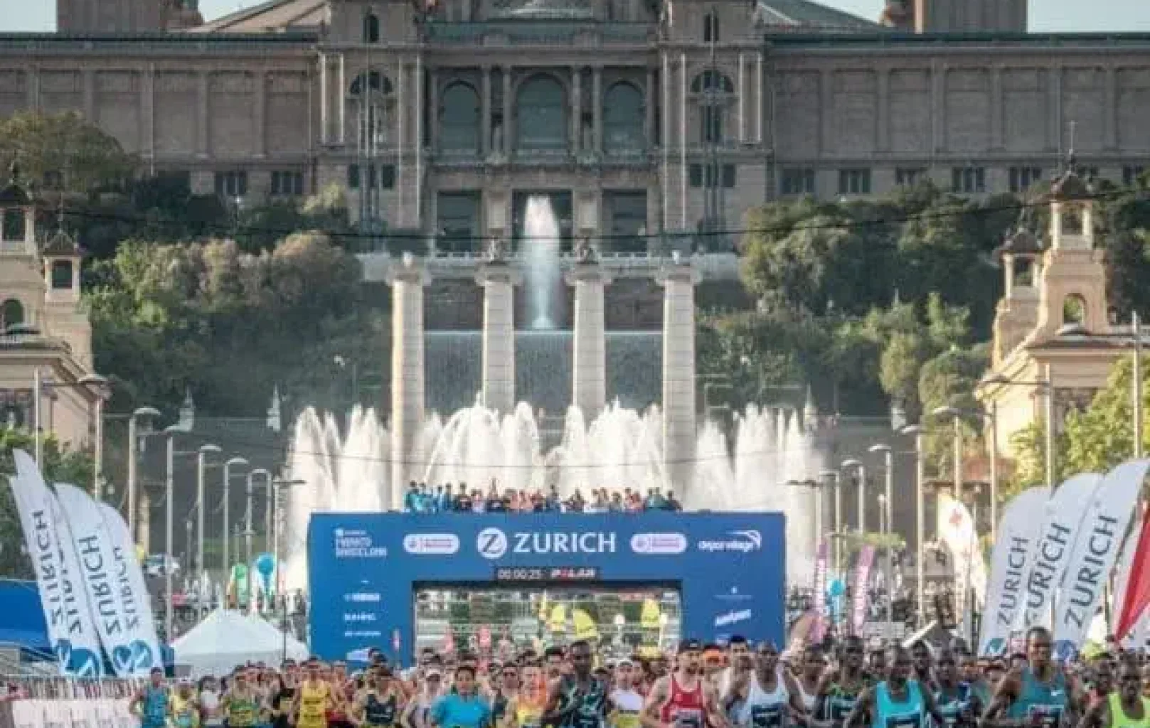 A large group of runners participates in a Zurich marathon event one brisk April morning, with fountains and a grand historic building in the background.