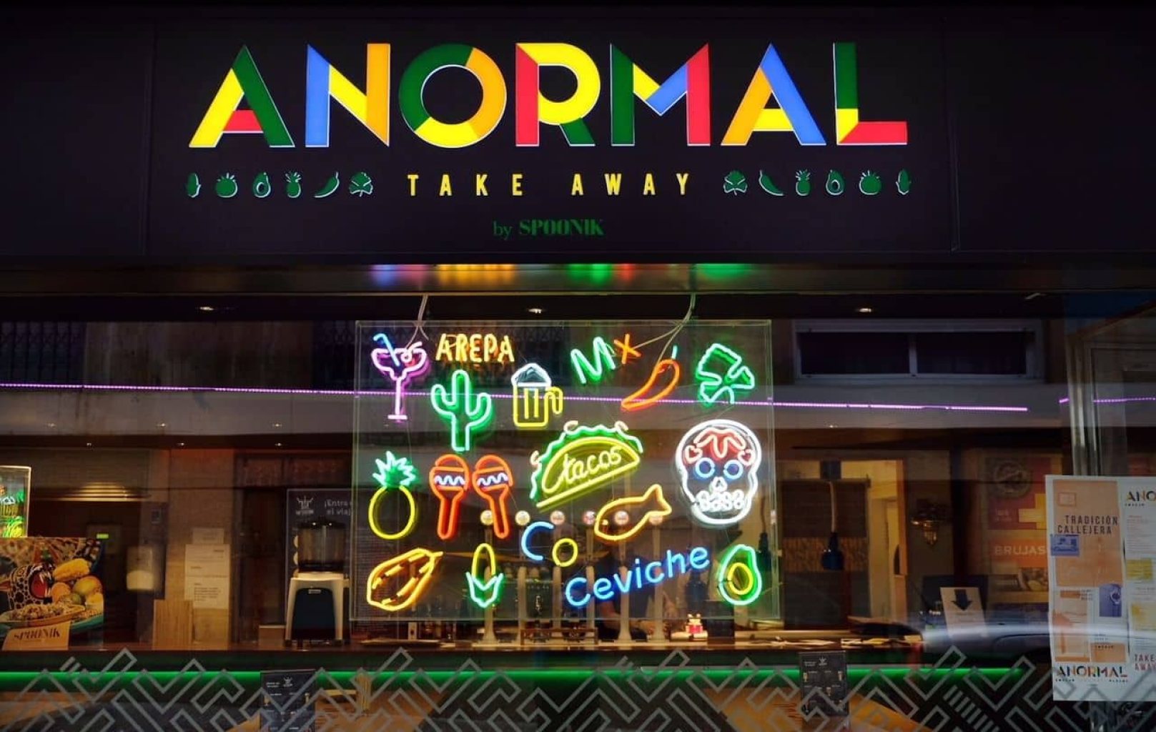El escaparate, con un cartel que reza "ANORMAL TAKE AWAY", luce dibujos de neón de colores de los platos favoritos de Anormal Food -platos mexicanos como tacos, arepas y ceviche- que iluminan el escaparate.