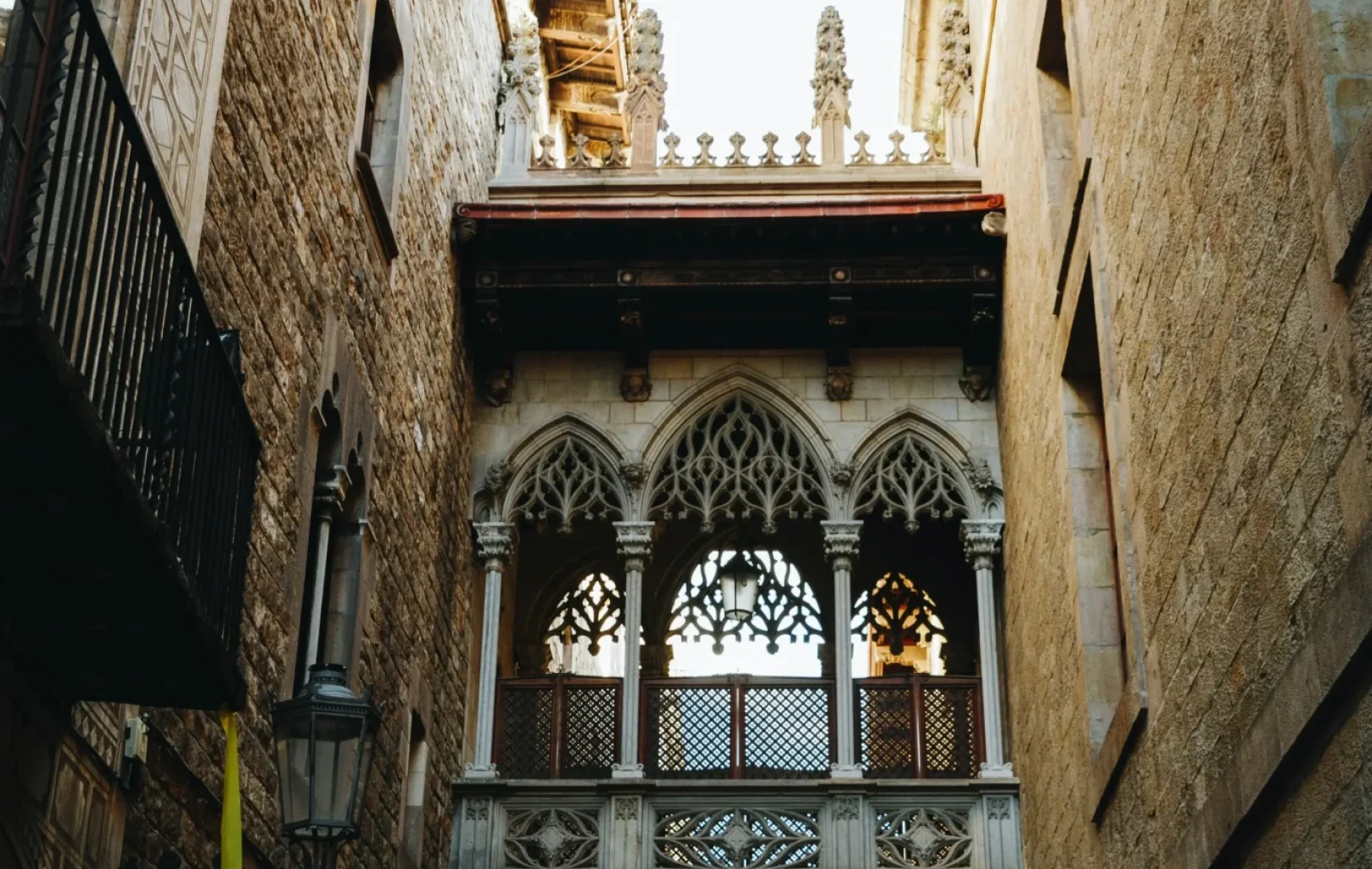 Un carrer estret amb edificis alts de pedra presenta un pont cobert ornamentat d'estil gòtic que connecta les estructures que hi ha per sobre del carrer.