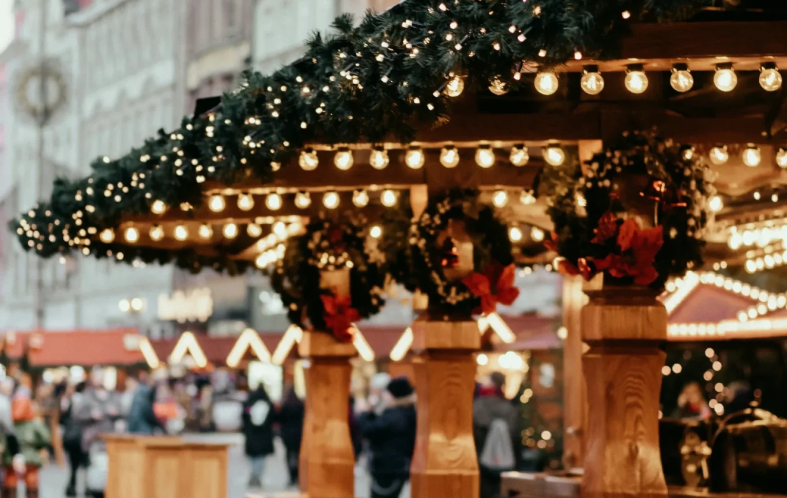 Outdoor Christmas market with decorated wooden stalls, string lights, and people walking in the background on a cobblestone street in Prague’s Wenceslas Square.
