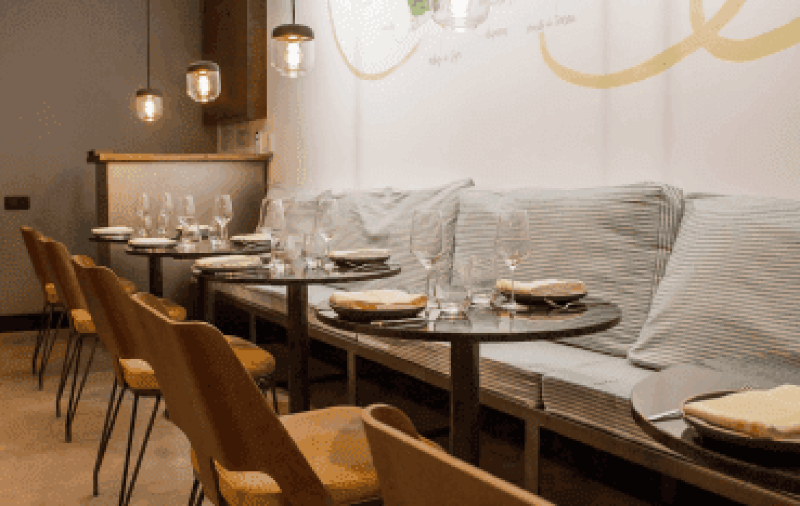 Moderno interior de restaurante en La Tartareria con pequeñas mesas redondas con platos y vasos, sillas marrones y un banco acolchado junto a la pared bajo luces colgantes.