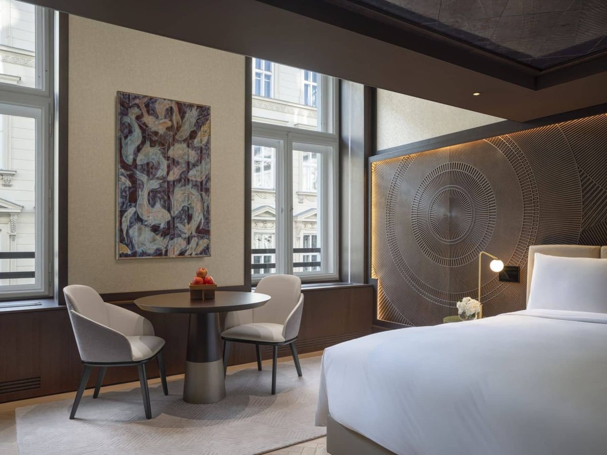Modern Almanac Deluxe hotel room with a large bed, round table and chairs, wall art, decorative headboard, and two windows. Natural light fills the space.