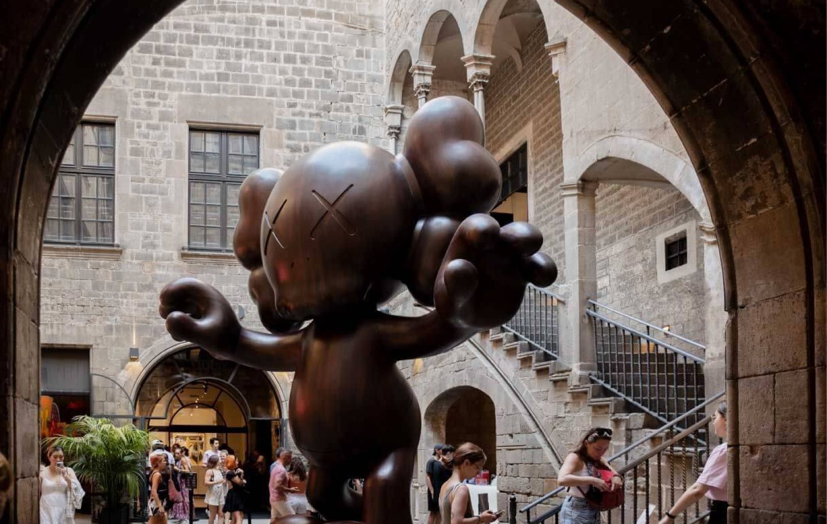 Una gran escultura de bronce de estilo caricaturesco -una llamativa pieza de arte contemporáneo- se alza en un histórico patio de piedra del Museo del Moco, mientras la gente pasea y se reúne a su alrededor en Barcelona.