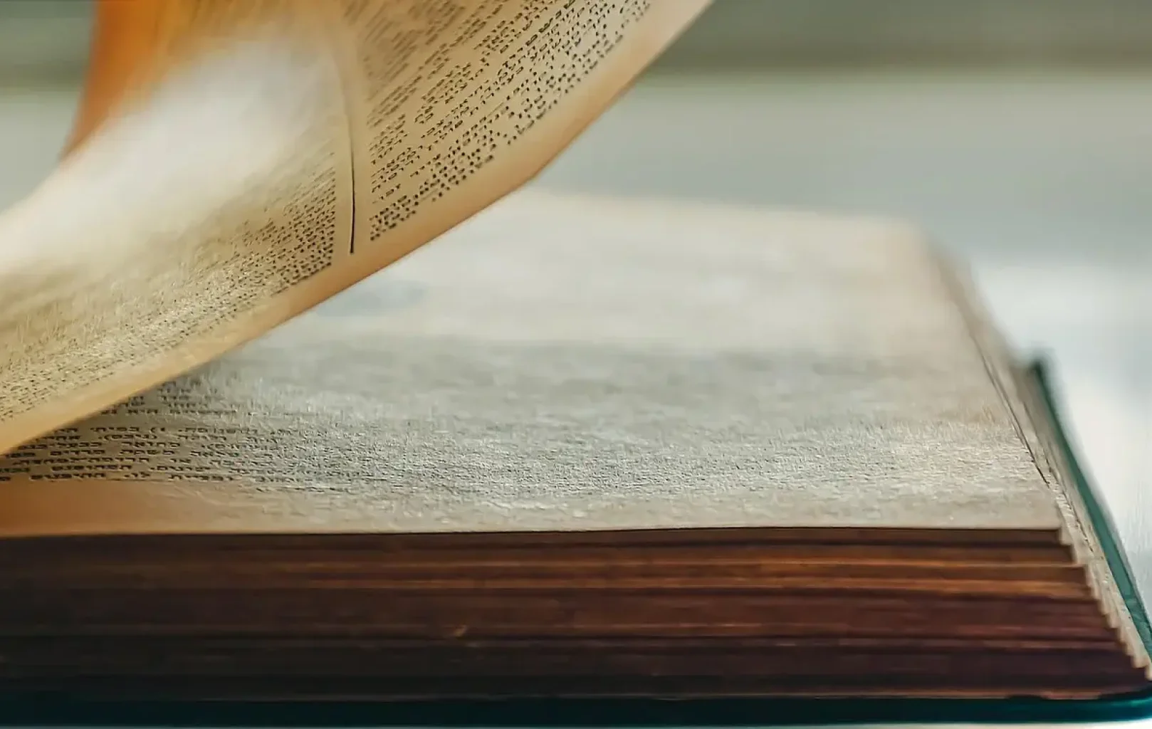 Detailní záběr na starou knihu se zažloutlými stránkami, jedna stránka je částečně otočená, je vidět starý papír a hustě potištěný text.