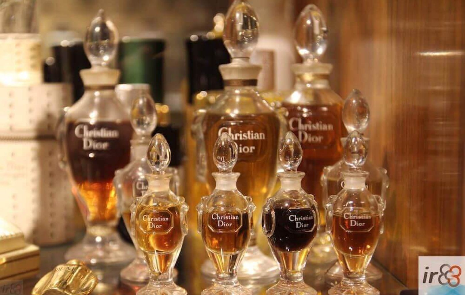 Varios frascos de cristal etiquetados como "Christian Dior" con distintos tonos de perfume líquido se exponen en una estantería con tapones ornamentados, que recuerdan a las exposiciones de fragancias de un museo de perfumes de renombre.