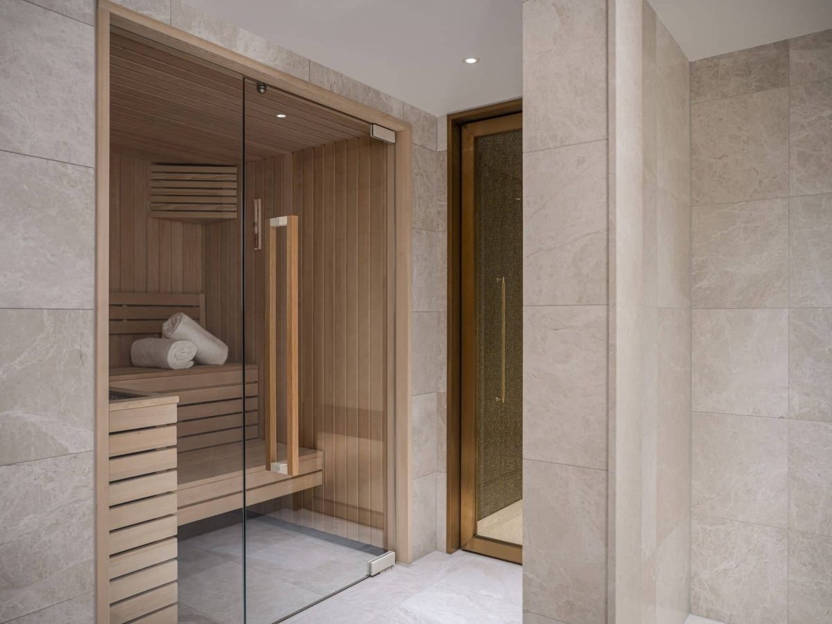 Modern spa area with a glass-enclosed wooden sauna, neatly rolled towels on a bench, and elegant Palais Floor tiles in neutral tones.